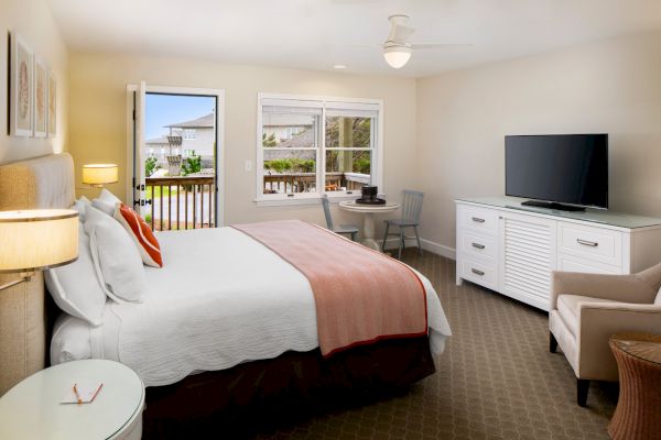 Sanderling Resort's neatly arranged guest hotel room with a large bed, TV, desk, chairs, and a balcony view.