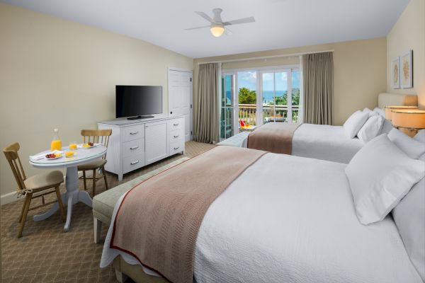 Sanderling Resort's tidy hotel guest room with two beds, a TV, ceiling fan, and sunset balcony view.