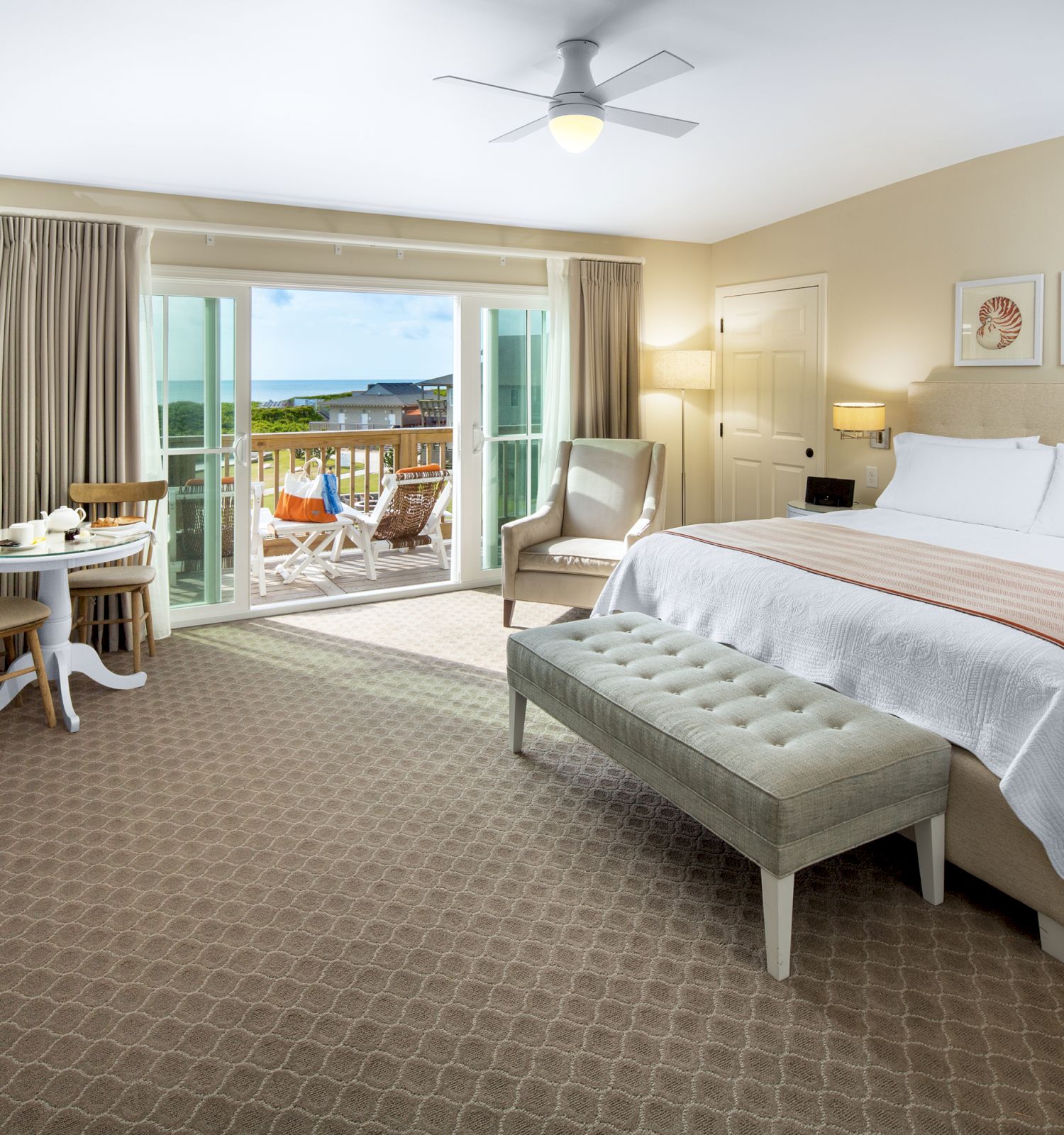 Sanderling Resort's well-lit hotel guest room with a large bed, furniture, and a balcony sunrise view of the Atlantic Ocean.