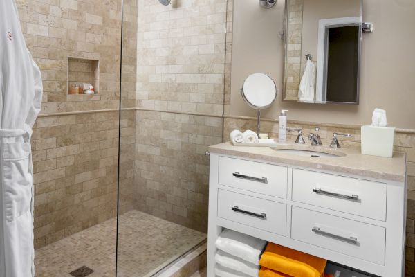 A modern bathroom with a glass shower, vanity cabinet, and towels.