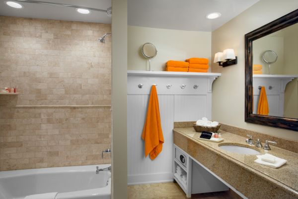 A clean bathroom with a tub, sink, towels, and a mirror.